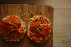 Zoomed out picture of two bagel slices with vegan creamy cheese and smoked carrot lox on top