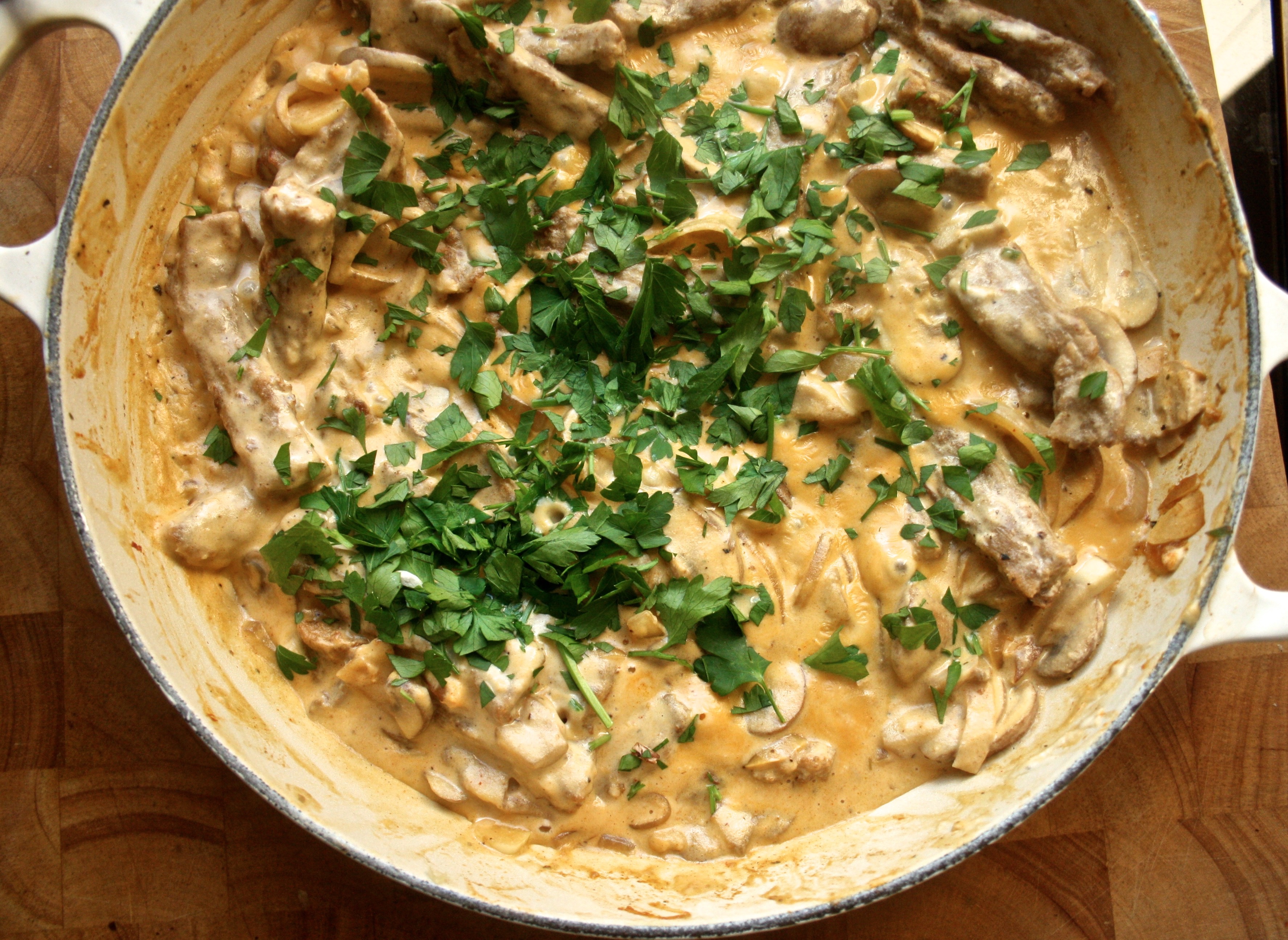A casserole dish with cooked vegan stroganoff inside topped with chopped parsley