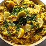 A large casserole dish full of vegan kedgeree topped with slices of lemon and herbs