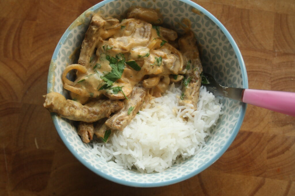 A bowl of vegan stroganoff served with white rice on top of a wooden work surface