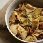 Vegan mushroom ragu with pappardelle pasta in a bowl on top of a wooden chopping board