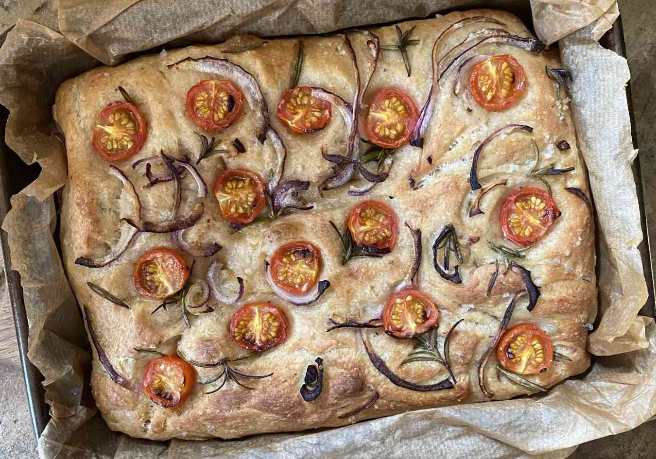 A tray of freshly cooked vegan spelt focaccia topped with tomatoes and onions