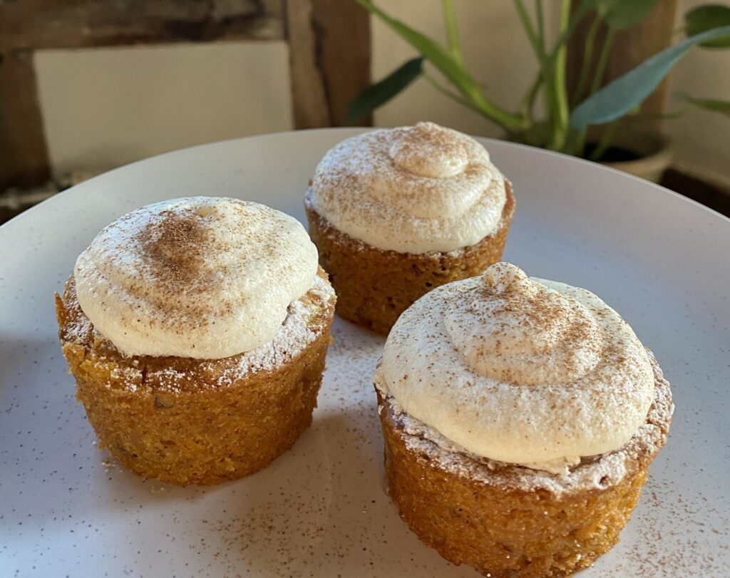 A plate of vegan carrot cake muffins with cream cheese in front of a plant