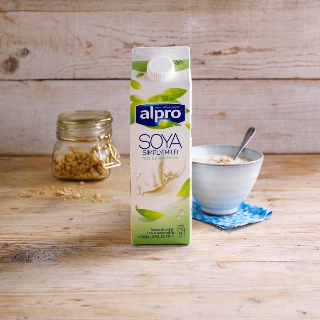 A carton of Soya plant-based milk by Alpro on a wooden surface next to some vegan food