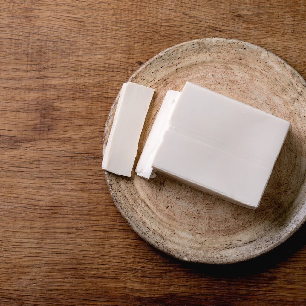 A block of sliced silken tofu on a plate on top of a wooden work surface