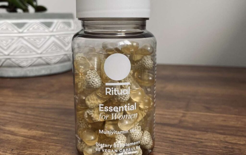 4. A close up of the ritual multivitamin capsules with vegan omega-3 that I reviewed next to their bottle on top of a wooden table