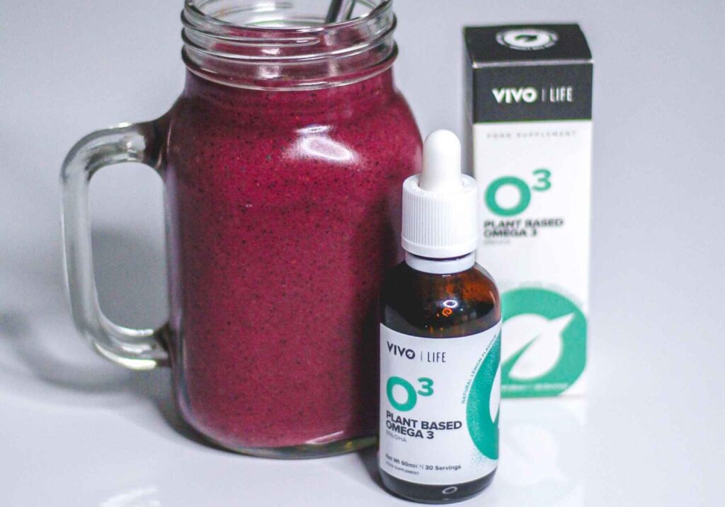 A jar of vegan omega-3 supplement from Vivo Life in liquid form next to a fruit smoothie