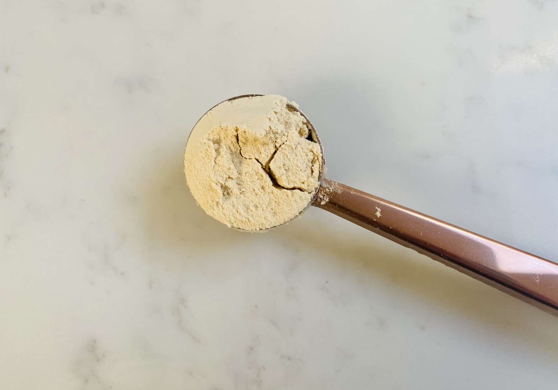 A rose metal spoon with a scoop of one of the best vegan protein powders sat on a marble work top