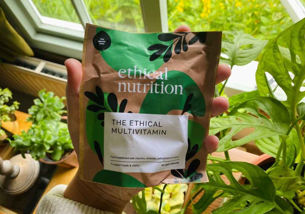 A bag of vegan multivitamins by Ethical Nutrition being held up to the camera in front of plants