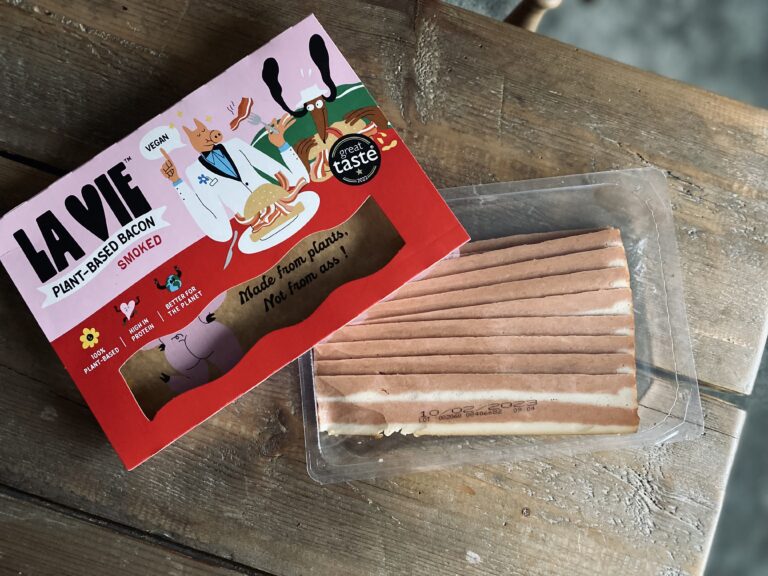 La vie vegan bacon packet next to the uncooked vegan bacon slices on a wooden table