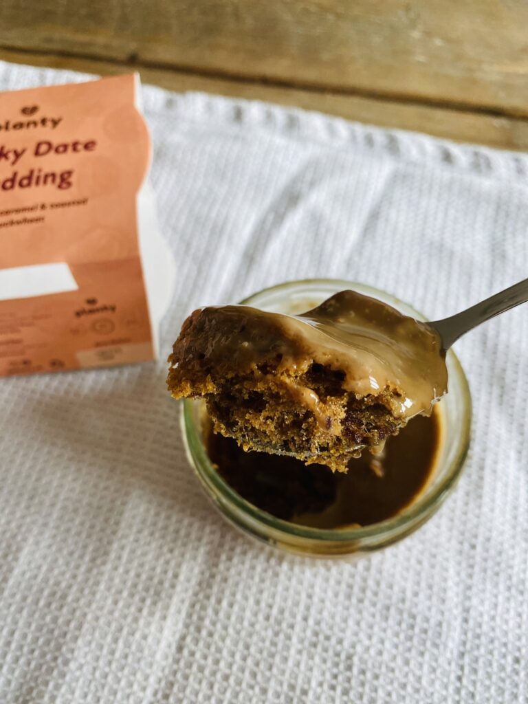 A close up of a spoonful of sticky date pudding from Planty infront of its packaging
