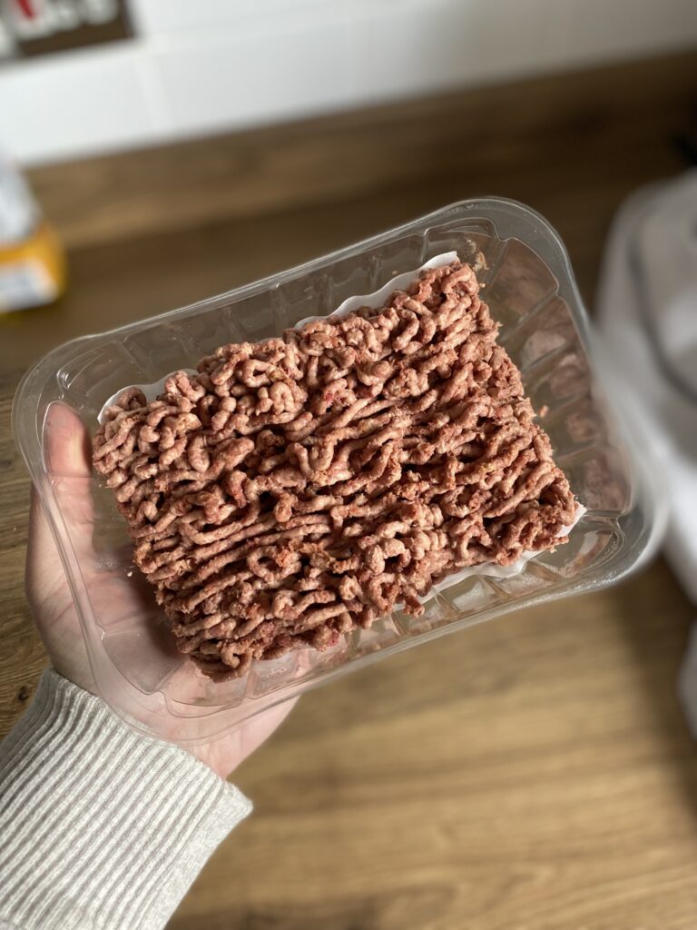 A packet of vegan mince meat being held up above a wooden kitchen counter top