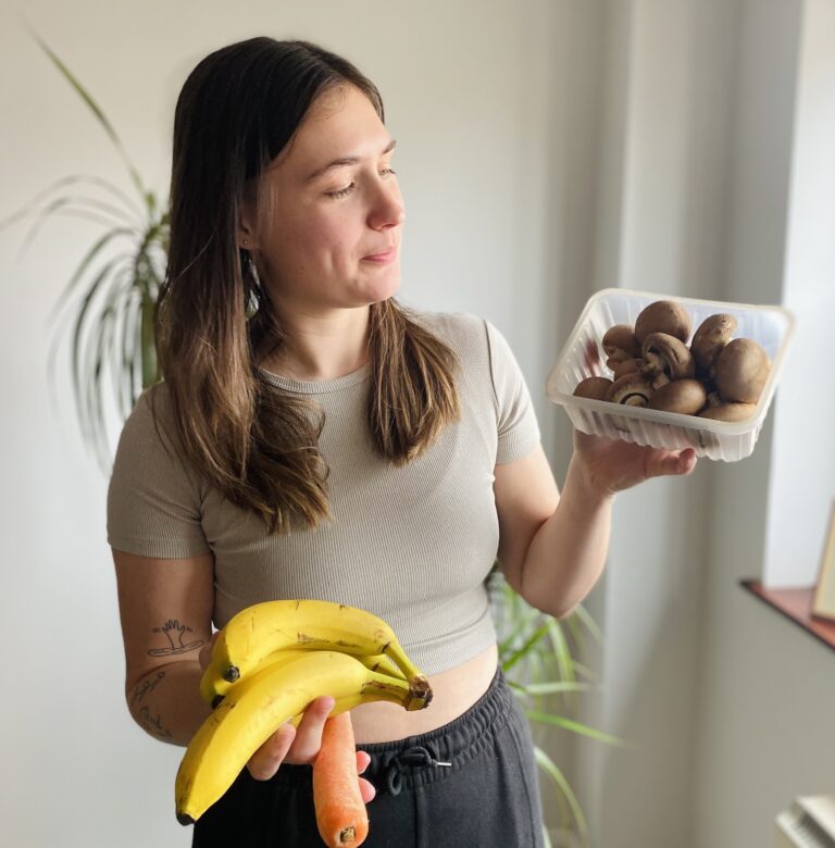 Lucy holding an array of vegan food in her hands whilst looking at the mushrooms
