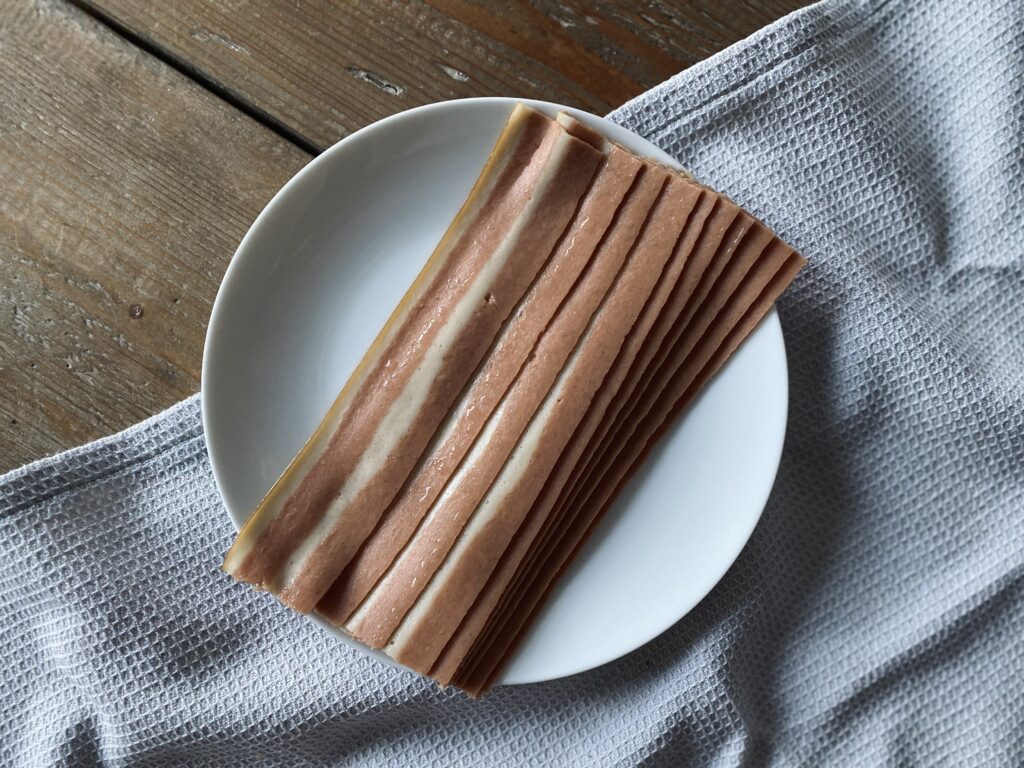 A plate of uncooked vegan bacon rashers on top of a towel on a wooden table