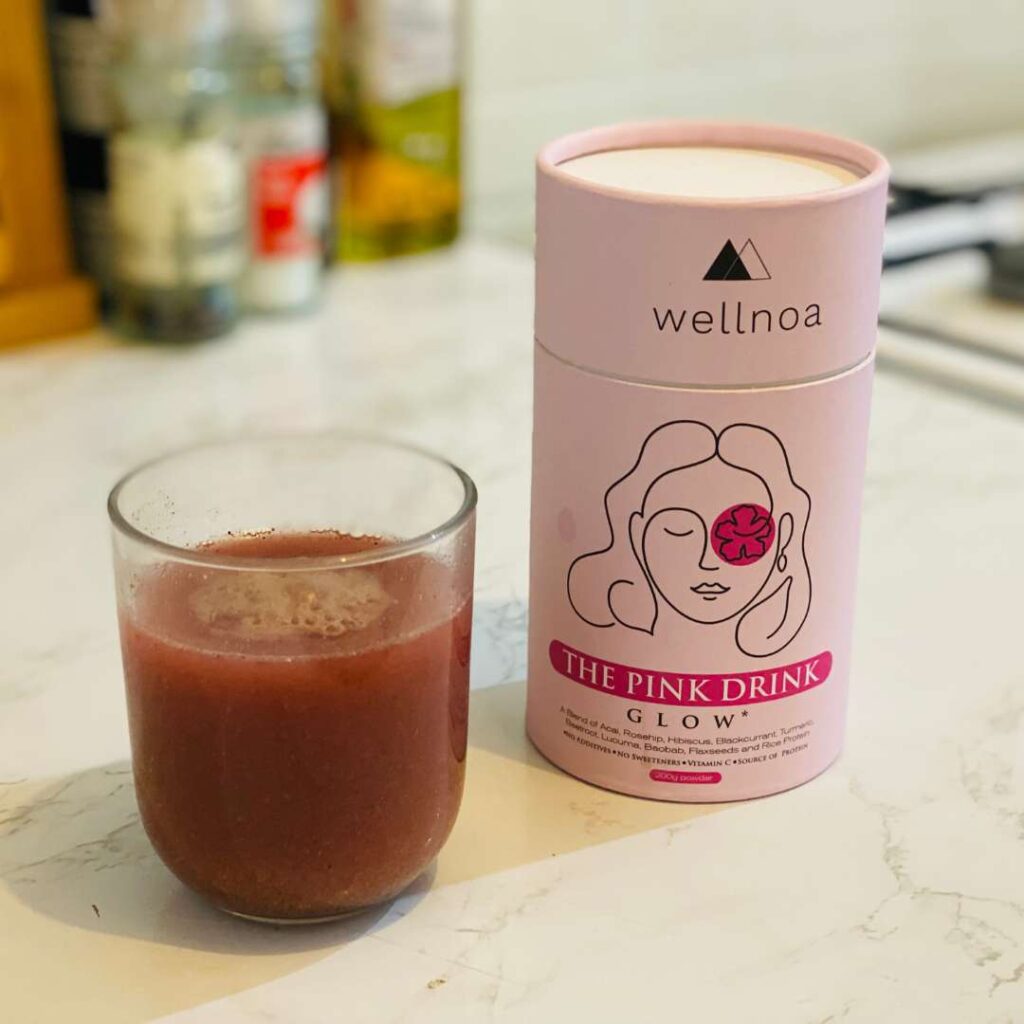 A tub of Wellnoa vegan superfood powder for skin next to a made up drink on top of a white kitchen surface