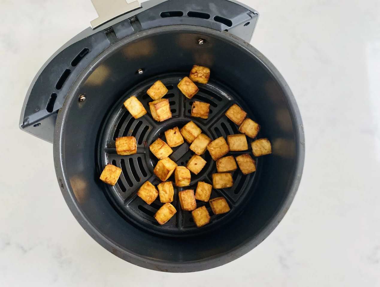 Cooked tofu inside the tray of one of the best air fryers on top of a marble kitchen work top