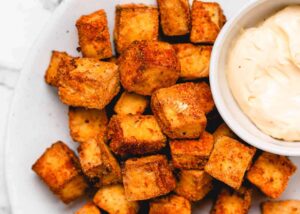 A plate of crispy vegan air fryer tofu next to a bowl of vegan mayonnaise