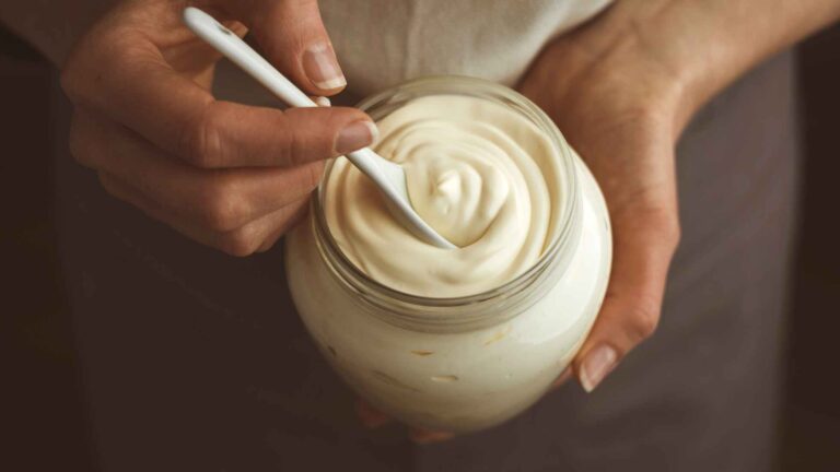 A woman holding a jar of vegan mayo about to take a spoon out