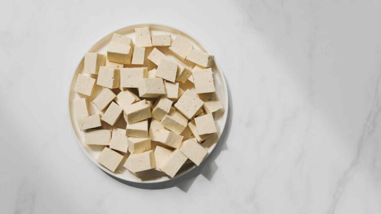 Blocks of tofu pilled up on a plate on top of a marble work surface