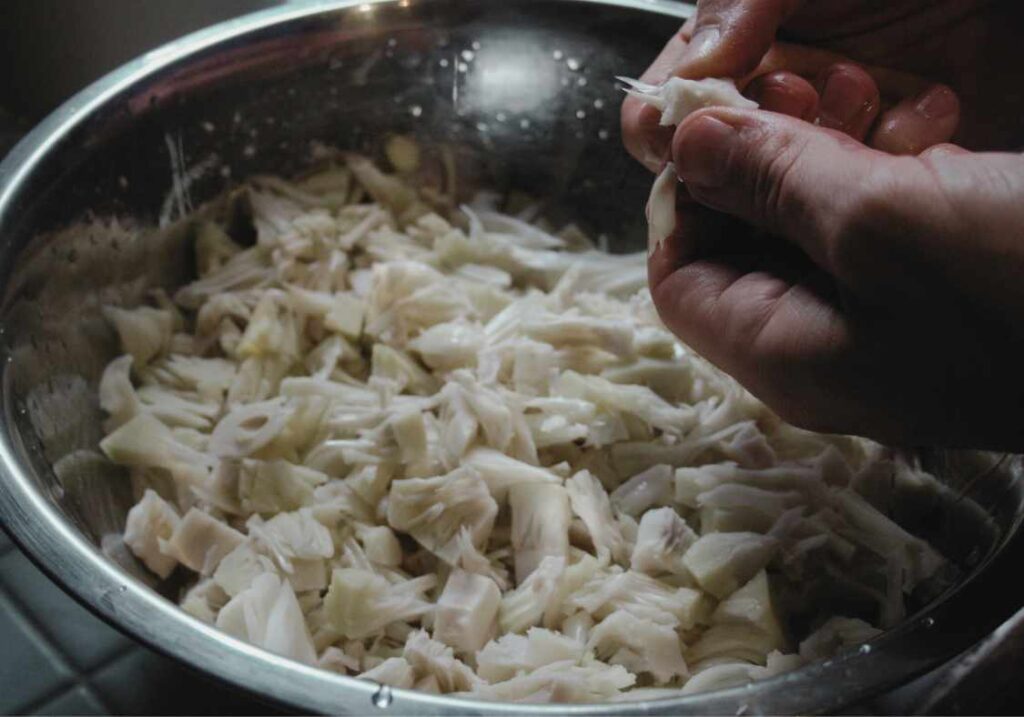 A bowl of young jackfruit that is being peeled part ready to be cooked