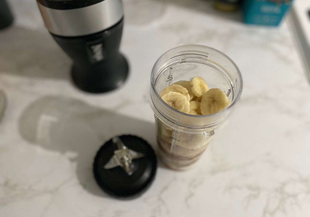 A Ninja blender cup with ingredients inside stood up on a marble style kitchen worktop with other kitchen items blurred out behind, ready to be tested for this Nutri Ninja Blender review