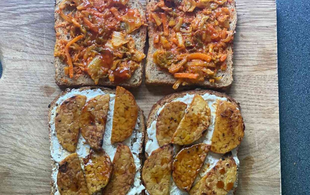 4 slices of bread which are being assembled with kimchi, tempeh and vegan cheese to create a vegan kimchi toastie