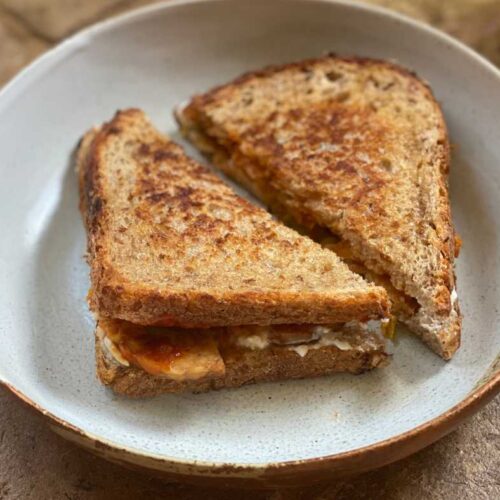 Two slices of vegan kimchi toastie on a earthy plate on top of a brick floor