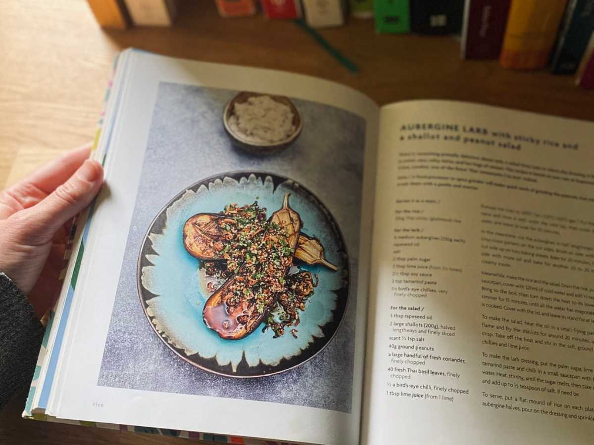 A recipe open in a vegan cookbook in front of many other vegan cookbooks on a shelf
