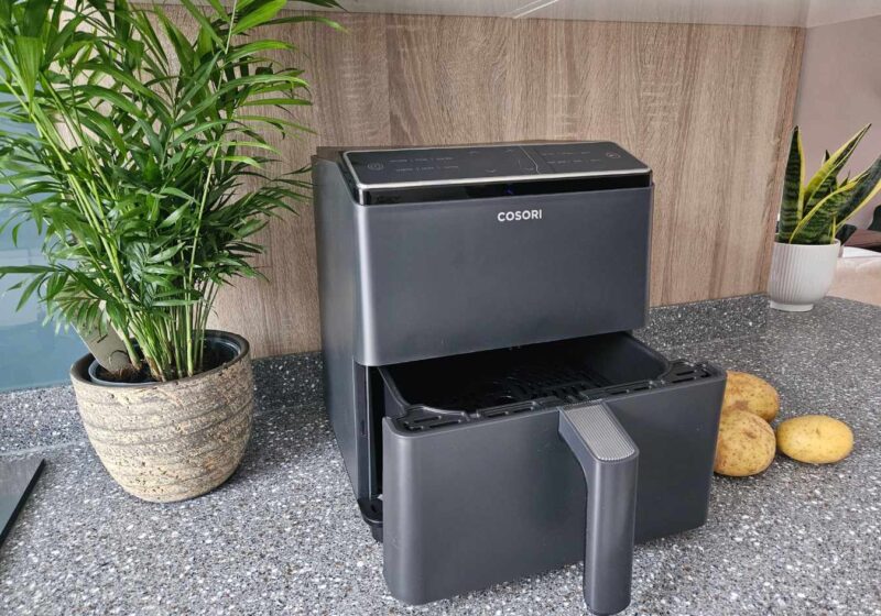 An air fryer with the drawer open next to a plant and some potatoes
