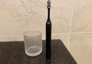 A black Suri toothbrush in front of a glass