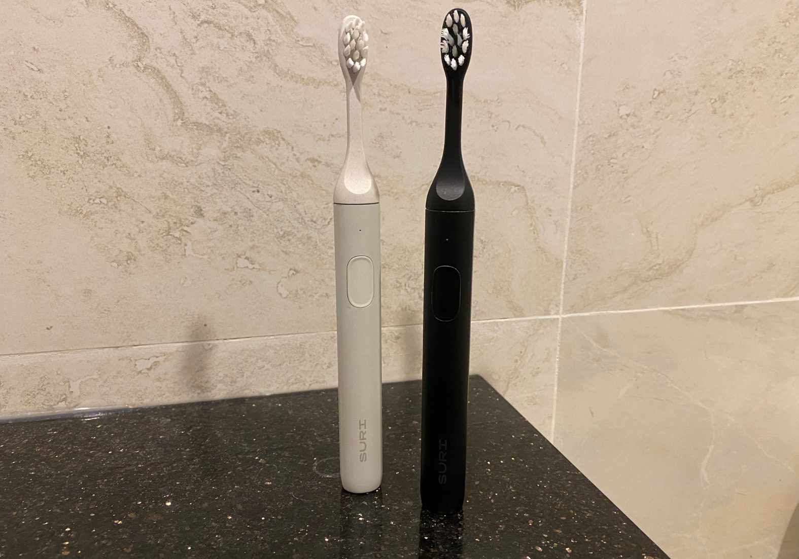 Two Suri toothbrushes next to each other on a bathroom shelf for this Suri toothbrush review