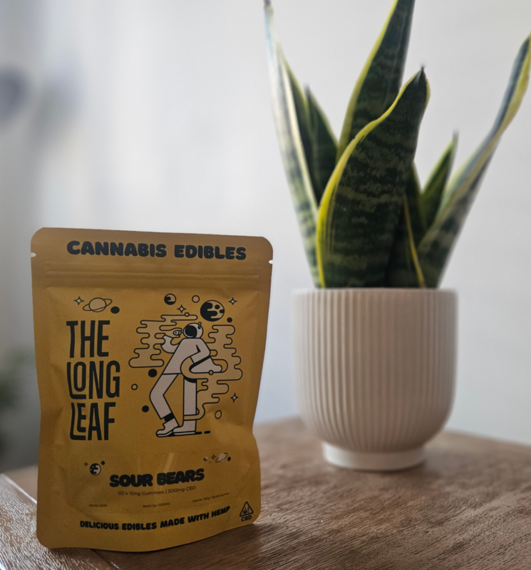 A bag of The Long Leaf CBD gummies in front of aplant