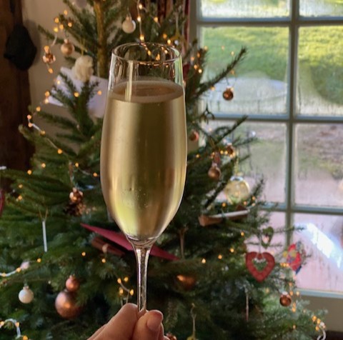 A glass of champagne in front of a Christmas tree surrounded by vegan christmas presents