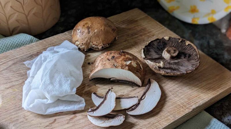 Some mushrooms on a chopping board next to a damp kitchen towel ready to be cleaned